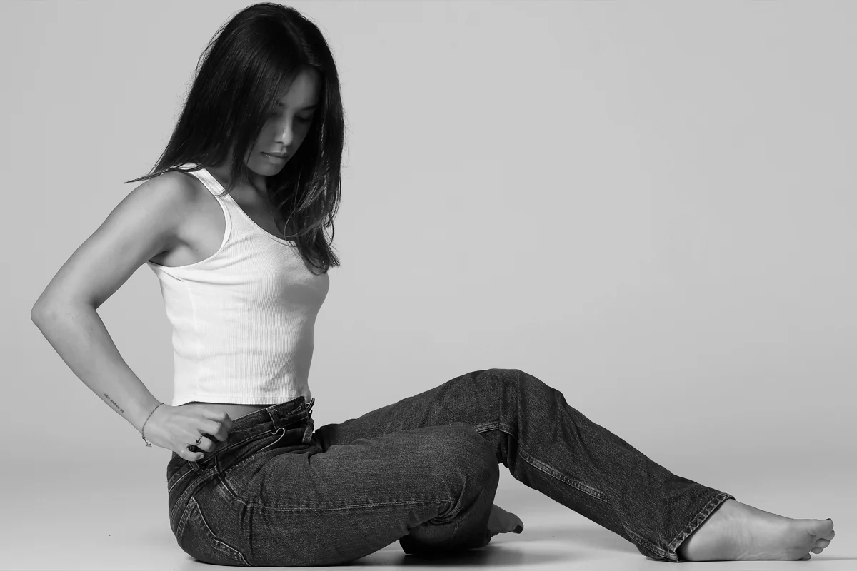 Femme assise portant un jean foncé et un débardeur blanc