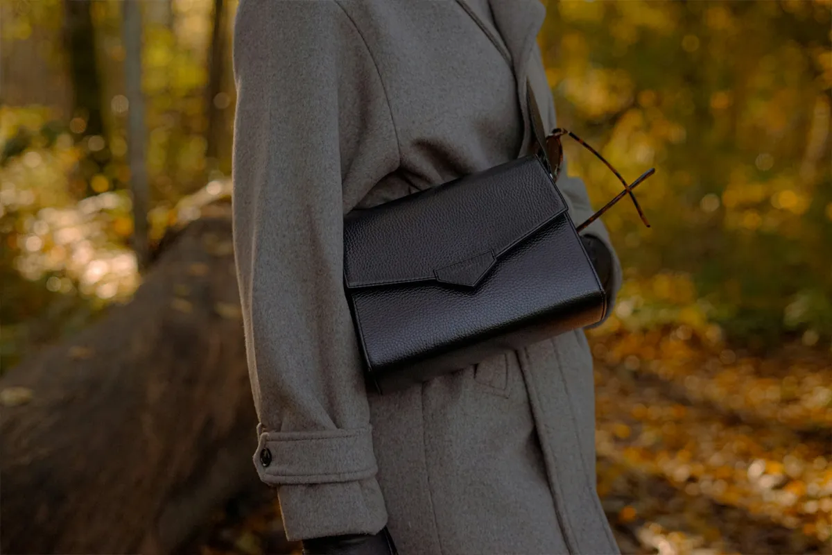 Sac à main noir en cuir grainé porté en bandoulière avec un manteau gris en automne