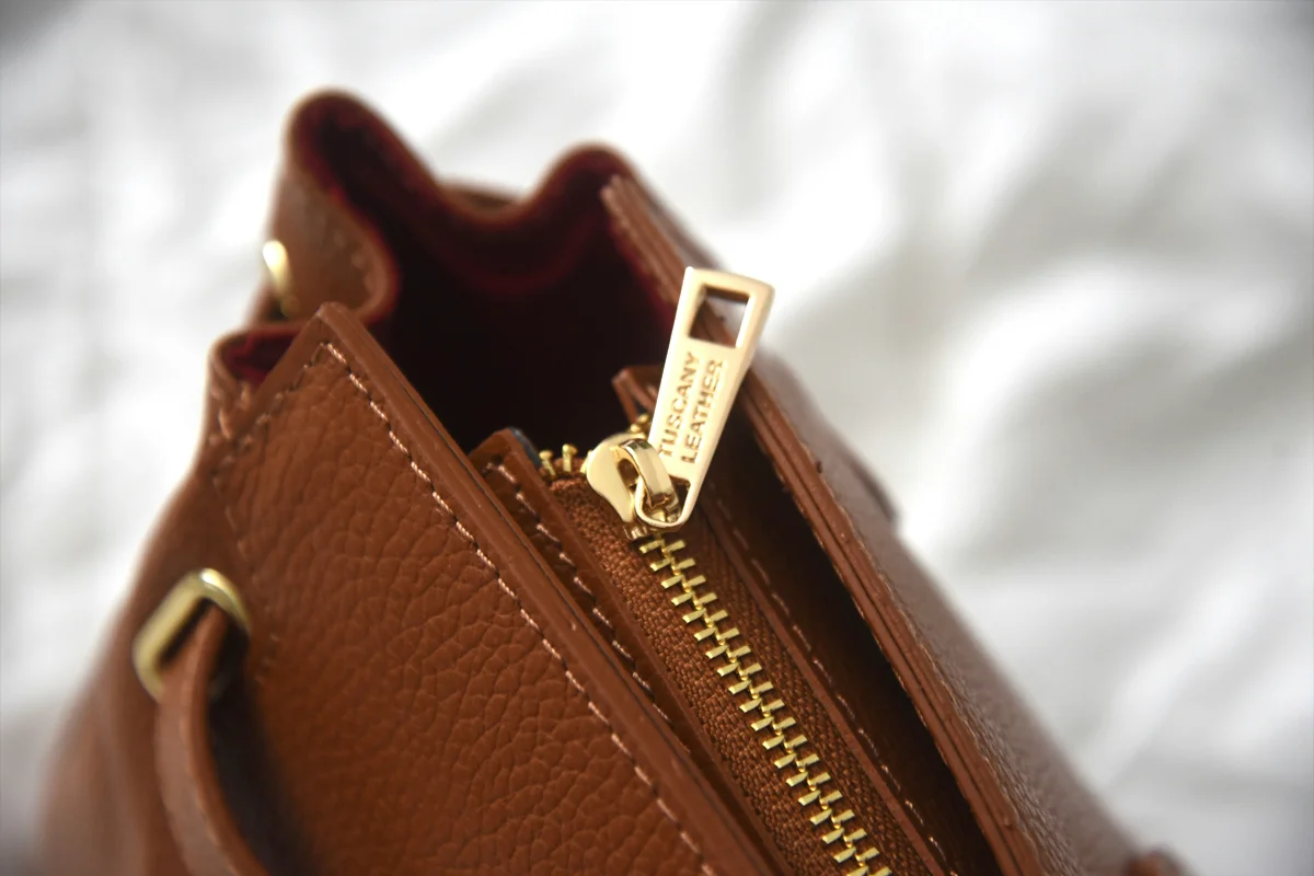 Détail de la fermeture éclair dorée et des coutures d'un sac à main en cuir marron