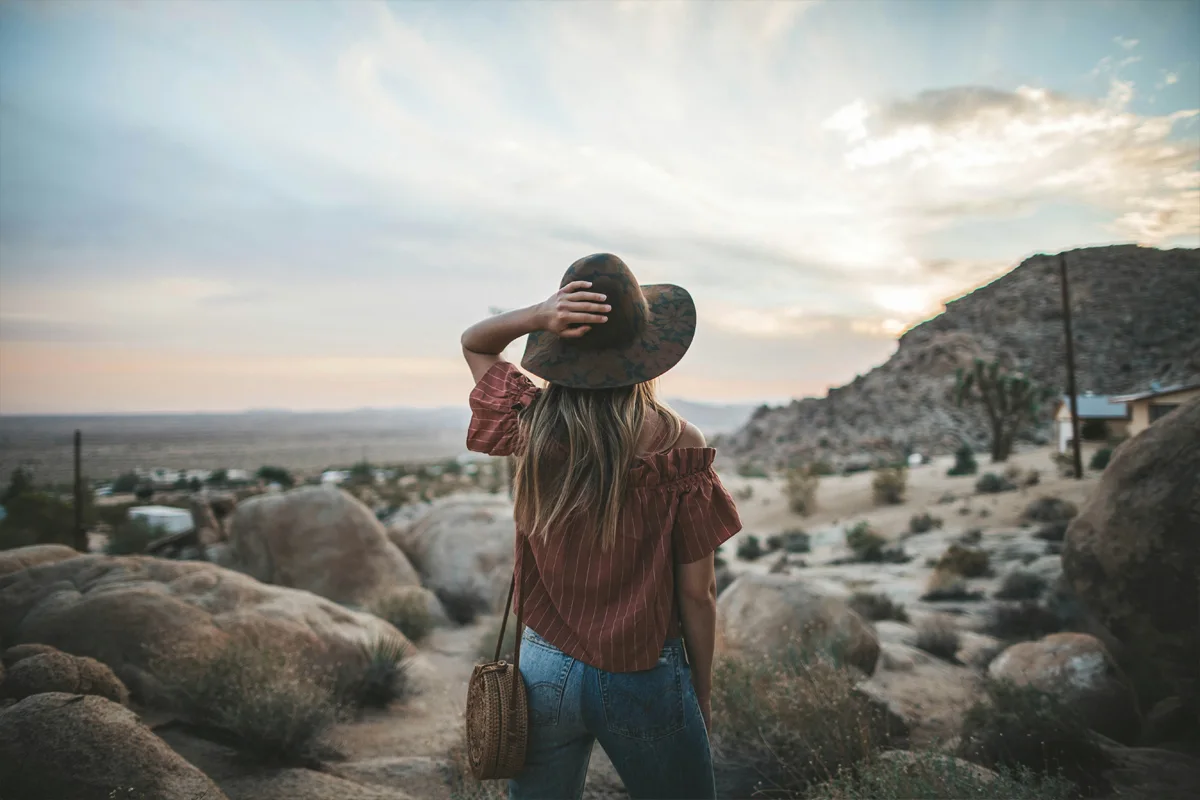 Femme portant un chapeau et un petit sac tressé en bandoulière dans un paysage désertique