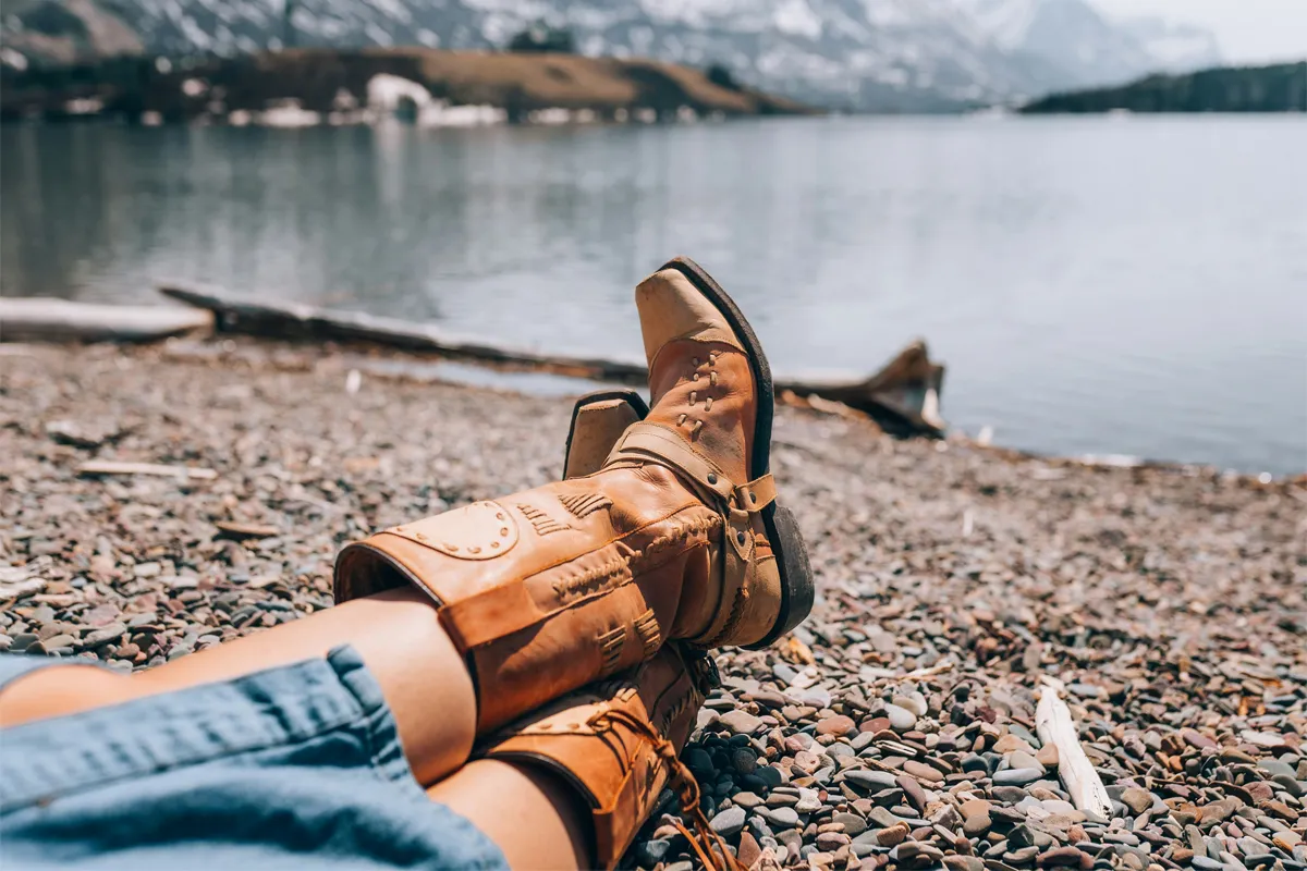Femme portant des santiags camel en cuir avec un jean, assise au bord d’un lac