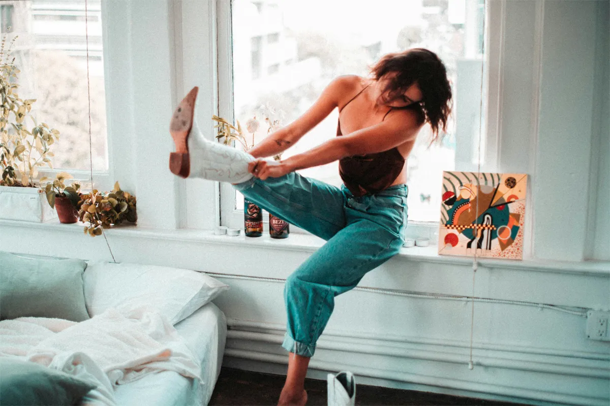 Femme en jean bleu essayant une santiag blanche brodée dans un intérieur lumineux