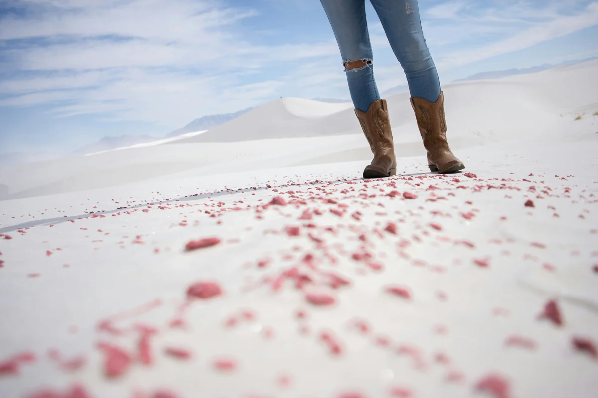 Femme portant un jean slim bleu et des santiags marron dans un paysage de dunes blanches