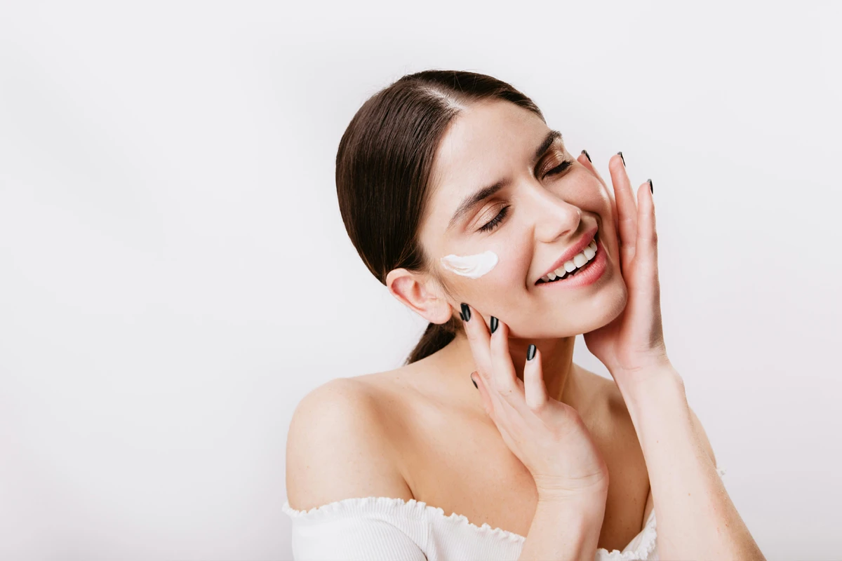 Jeune femme souriante appliquant une crème hydratante sur sa joue