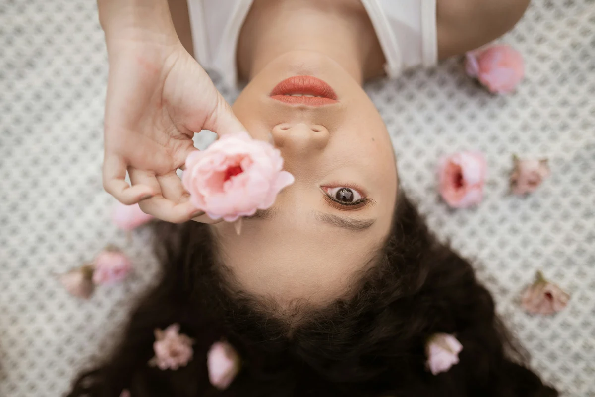 Portrait d’une femme allongée entourée de fleurs roses lors d’un rituel beauté
