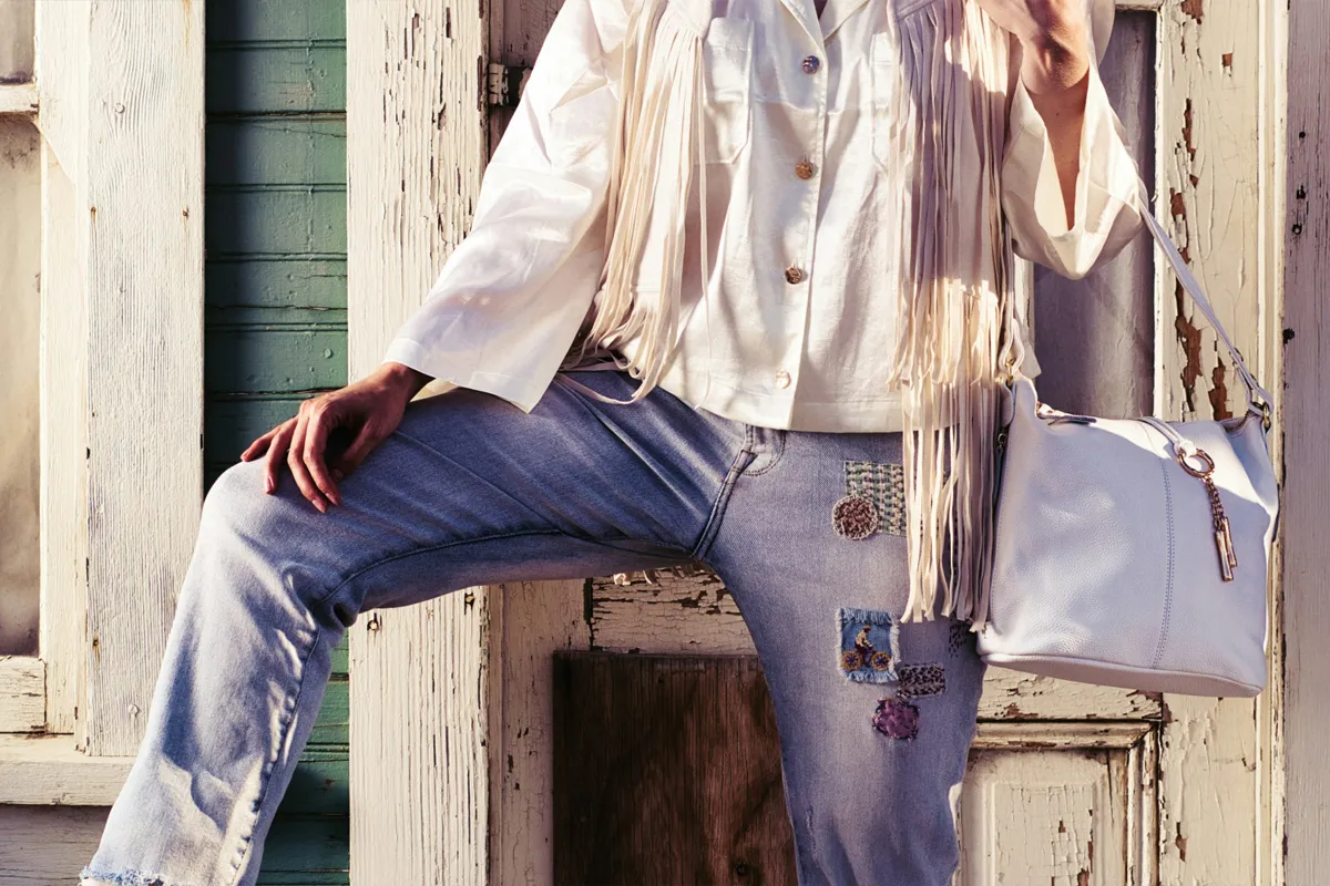 Look féminin décontracté avec jean bleu, chemise blanche, gilet à franges et sac à main blanc